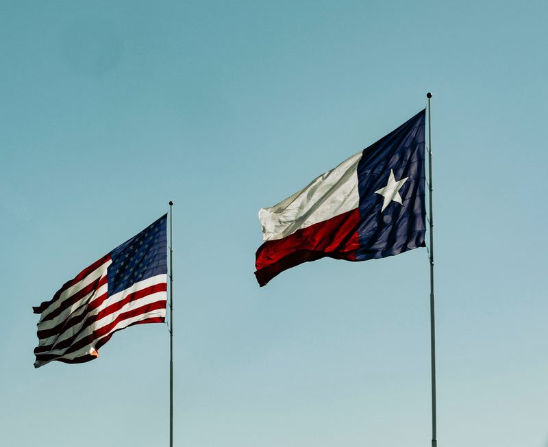Banderas de Texas y de EE. UU. ondeando bajo un cielo azul
